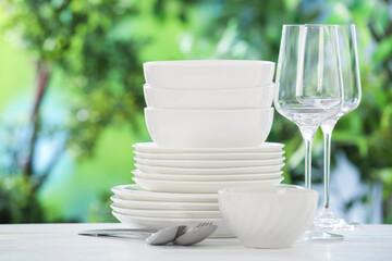 Different clean dishes on white table against blurred green background