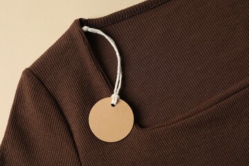 Brown garment with tag on beige background, top view
