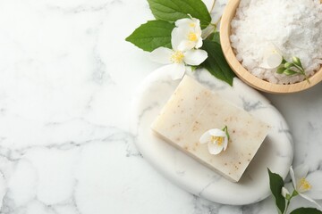 Soap bar, sea salt and jasmine flowers on white marble table, flat lay. Space for text