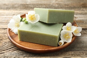Soap bars and jasmine flowers on wooden table, closeup