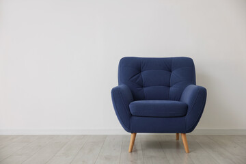 Comfortable blue armchair near white wall indoors, space for text