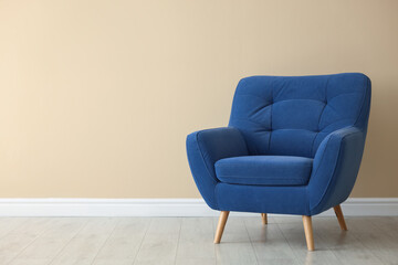 Comfortable soft blue armchair near beige wall indoors, space for text