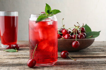 Tasty cherry soda with ice cubes, berries and mint on wooden table, closeup