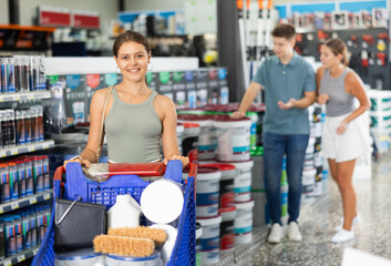 Woman shoppers stand with trolley filled with paint goods for repair and coloring in supermarkets...