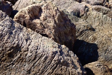 Textured coastal rocks with deep grooves and layers, shaped by centuries of wind and water erosion. The rugged surface contrasts with the soft shadows and sunlight.