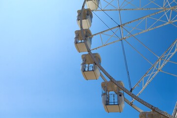 Obraz premium A close-up view of the cabins of a Ferris wheel against a vibrant blue sky on a sunny day. The white structure contrasts beautifully with the clear sky, creating a cheerful summer atmosphere, perfect