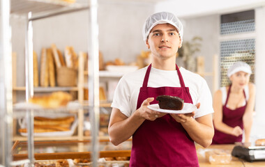 Young man seller holding basket with sweet piece of cake in bakery