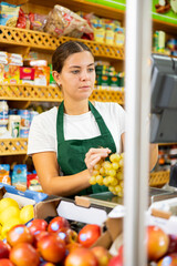 Smiling female shopping assistant weighing grapes in grocery shop