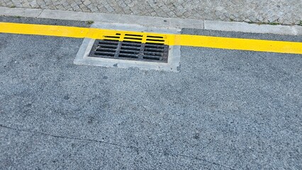Yellow traffic line next to storm drain on asphalt road
