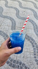 Blue Slush Drink with Red and White Straw Held Outdoors