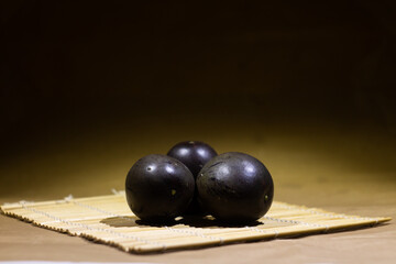 Three Dark Purple Passion Fruits on a Woven Bamboo Mat