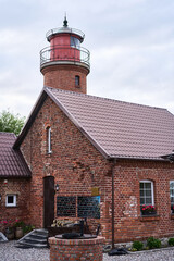A beautifully picturesque brick lighthouse situated right next to a charming rustic home, all set against a cloudy sky