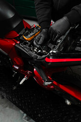 Mechanic testing battery with multimeter. Motorcycle battery is tested using digital multimeter to check voltage and health. Digital multimeter reads motorcycle battery voltage during inspection. © Rabizo Anatolii