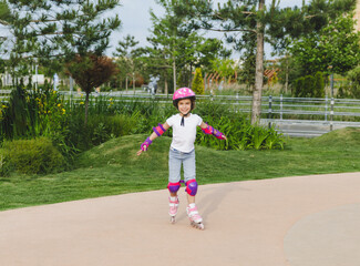 A little curly-haired girl rollerskates within the necessary facilities in the city. In a helmet...