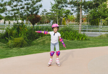 A little curly-haired girl rollerskates within the necessary facilities in the city. In a helmet...