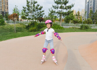 A little curly-haired girl rollerskates within the necessary facilities in the city. In a helmet...