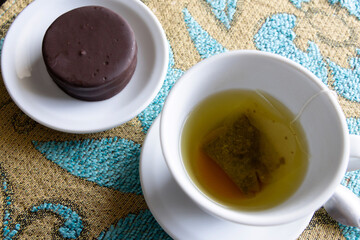 An alfajor inside a small plate next to a cup with tea.