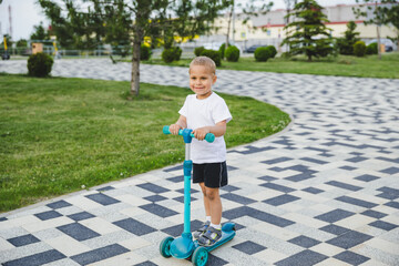 A boy of 4-5 years old rides a scooter in a city park.