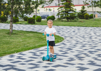 A boy of 4-5 years old rides a scooter in a city park.