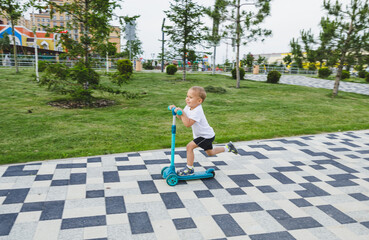 A boy of 4-5 years old rides a scooter in a city park.