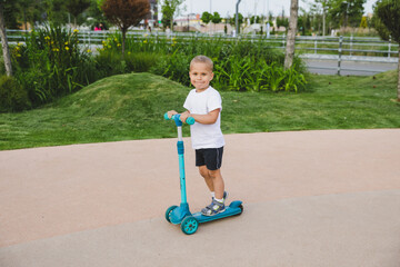 A boy of 4-5 years old rides a scooter in a city park.