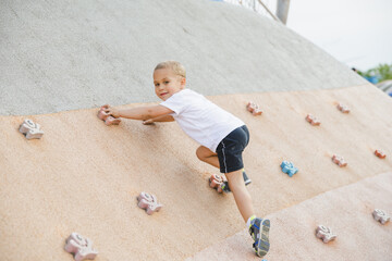 little boy climbing stone wall on playground. sport life concept