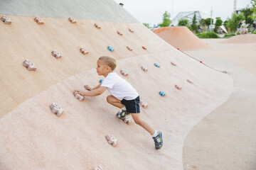 little boy climbing stone wall on playground. sport life concept