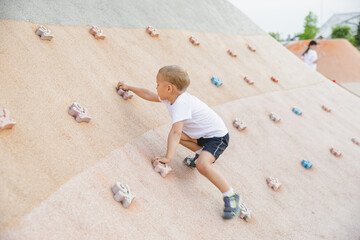 little boy climbing stone wall on playground. sport life concept