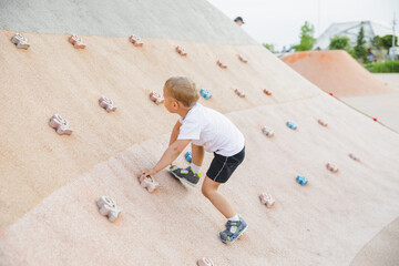 little boy climbing stone wall on playground. sport life concept