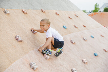 little boy climbing stone wall on playground. sport life concept