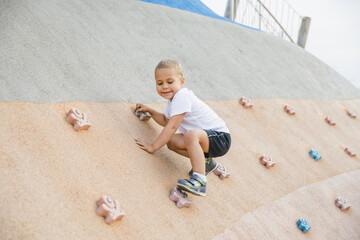 little boy climbing stone wall on playground. sport life concept