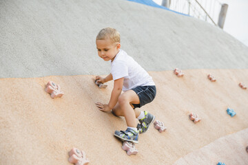 little boy climbing stone wall on playground. sport life concept