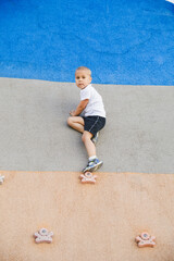 little boy climbing stone wall on playground. sport life concept