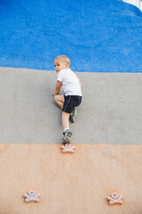 little boy climbing stone wall on playground. sport life concept