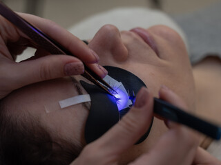 A woman undergoing eyelash extension procedure using an ultraviolet lamp.