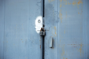 A weathered blue metal door with peeling paint features a rusty lock securing it closed in an abandoned industrial location