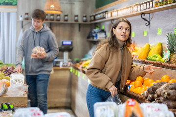 Young woman in casual clothes buys tangerines in greengrocer's shop