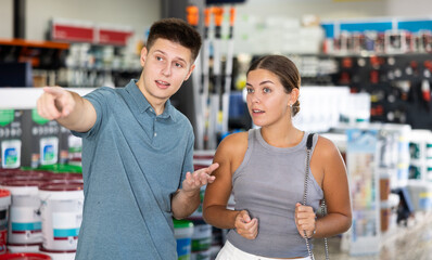 Young positive woman and man shopping in big building store, man pointing to something