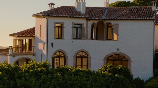luxury Mediterranean villa from a distance, perched on a hill with stunning ocean views, whitewashed wells, terracotta roof, large windows reflecting the sunlight lush greenery surrounding the villa