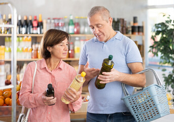 Couple of elderly man and elderly woman choosing olive or sunflower oil in bottle in grocery store