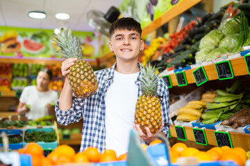 Confident guy buyer who came to a vegetable store for shopping, chooses pineapple near the counter