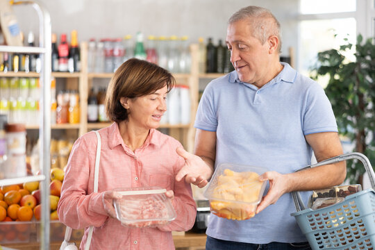 Mature spouses man and woman customers in meat department of store took raw chicken carcass and pork meat from shelf, examines product, makes purchase decision, thinks about desired type of meat. - Powered by Adobe