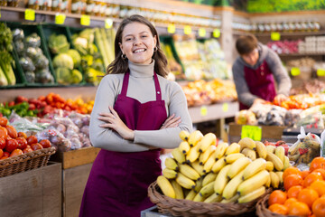 Young woman seller in apron lays out bananas on counter in vegetable shop