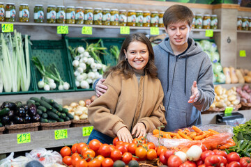 Happy young couple buying together tomatoes in large fruit and vegetable market