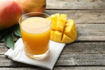 Tasty mango juice in glass, fresh fruits and green leaves on wooden table, closeup. Space for text