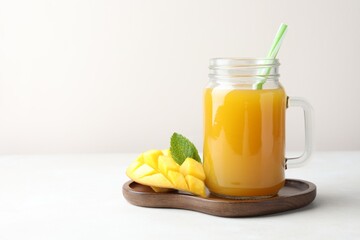 Tasty mango juice in glass mason jar, fresh fruit and mint on white table, space for text