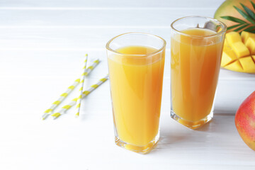 Tasty mango juice in glasses, fresh fruits, straws and green leaves on white wooden table, closeup