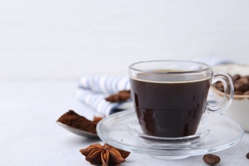 Cup of aromatic coffee, beans and star anise on white table, closeup. Space for text