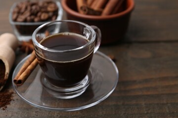 Refreshing coffee in cup and cinnamon stick on wooden table, closeup