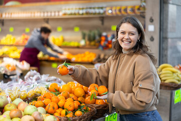 Happy young girl chooses and buys ripe delicious tangerines in grocery section of the supermarket